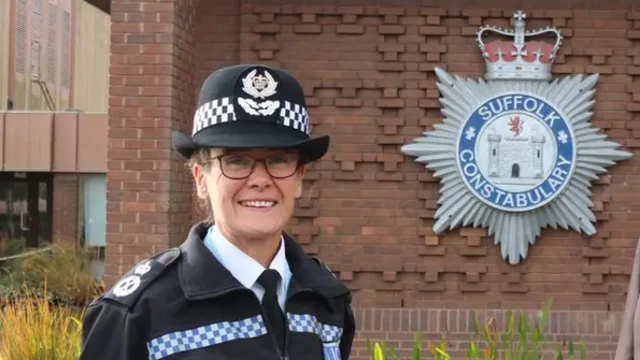 Rachel Kearton, con uniforme de policía, frente a la sede de la Policía de Suffolk. El logotipo de la policía se puede ver detrás de ellos, en un muro de ladrillos, frente a un estanque ornamental.