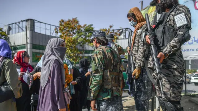 Seorang pengunjuk rasa perempuan yang mengenakan jilbab sedang berbicara dengan seorang penjaga Taliban