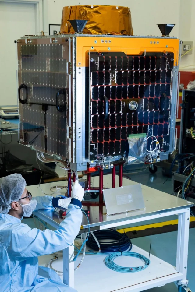 فردی با لباس مخصوص در حال کار روی یک قطعه از ماهواره