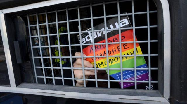 Un activista ruso de los derechos de los homosexuales y LGBT muestra un cartel que dice "El amor es más fuerte que la homofobia" desde el interior de una furgoneta de la policía antidisturbios rusa.