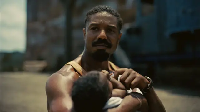 Michael B Jordan, con una camiseta tipo esqueleto, sostiene a un bebé. 
