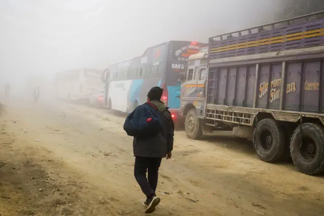 दाउन्ने क्षेत्रमा सडक अवरुद्ध भएपछि राजमार्गमा अलपत्र परेका सवारीसाधननजिकै बाटोमा हिँड्दै केही मानिसहरू