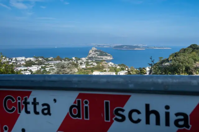 Placa de trânsito com a inscrição cidade de Ísquia, ao fundo o castelo aragonês