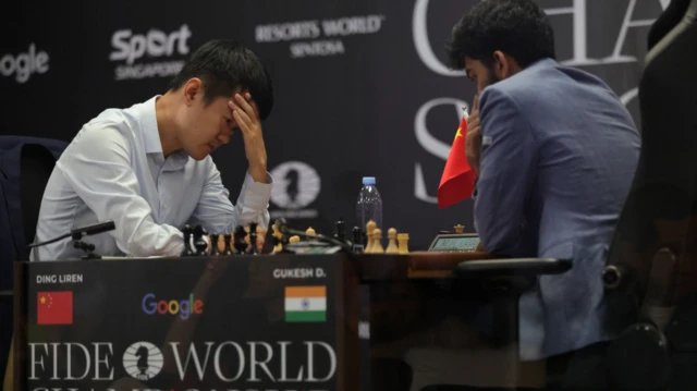 Ding Liren se lleva las manos a la cabeza mientras juega contra Gukesh Dommaraju. Los dos jugadores se encuentran uno frente al otro en el tablero de ajedrez.