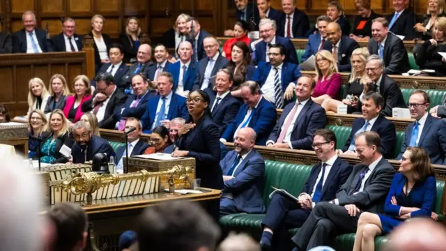 下院本会議室で、多くの保守党議員が緑のベンチに座るのを前に、「ディスパッチボックス（公文書箱）」に書類を置き、胸に右手を当てながら発言するベイドノック氏。議員の多くは党首の発言を受けて笑っている