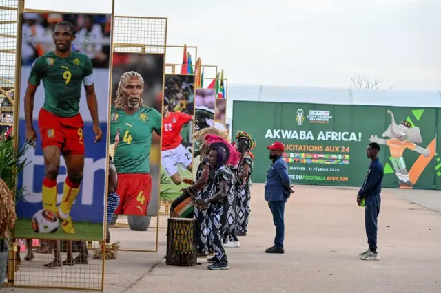 Des artistes ivoiriens jouent du tambour à côté des tribunes portant les photos des anciens joueurs de football camerounais Samuel Eto'o (G) et Rigobert Song (2e G) avant le tirage au sort officiel de la Coupe d'Afrique des Nations (CAN) 2024 au Parc des Expositions d'Abidjan, dans le sud-est de la Côte d'Ivoire, le 12 octobre 2023.
