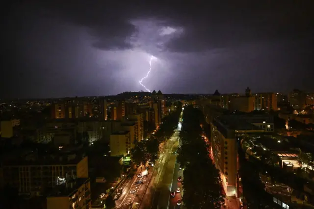 صاعقة برق في منطقة الأعمال التجارية لا ديفونس خارج باريس، الصورة التقطت ليلاً حيث مجموعة مبانٍ سكنية وسيارات وسماء سوداء مليئة بالغيوم وتظهر وسطها صاعقة برق.