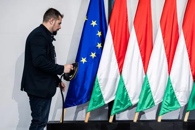 Bir adam Macaristan bayraklarının yanındaki AB bayrağını ütülüyor. 