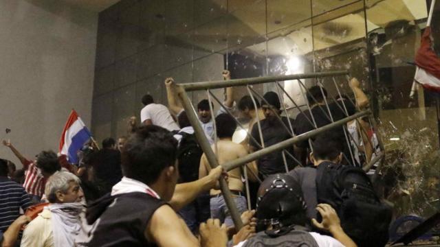 Manifestantes golpeando una entrada del Palacio Legislativo de Paraguay,