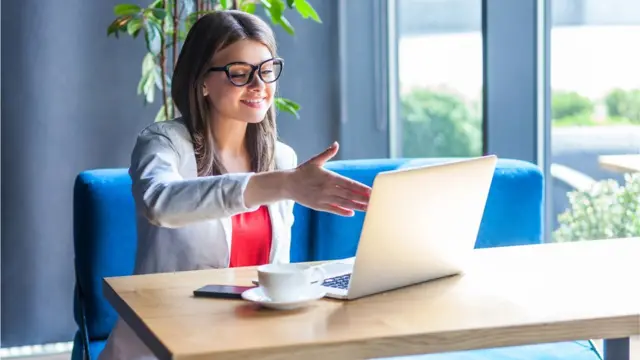 Mujer frente a una pantalla de computadora ofreciendo su mano.