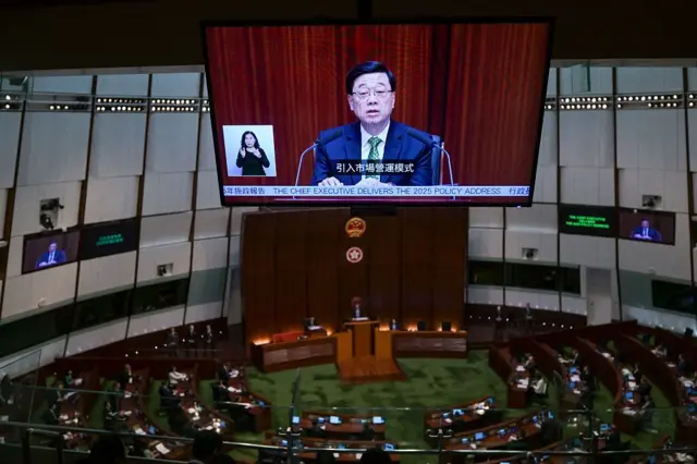 立法会的会议室内，大屏幕上展示香港特首李家超正发表新一份施政报告。