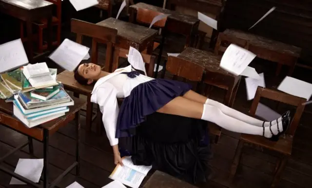 นักเรียนหญิงในชุดเครื่องแบบที่ต่างไปจากปกติ นอนบนโต๊ะในห้องเรียน