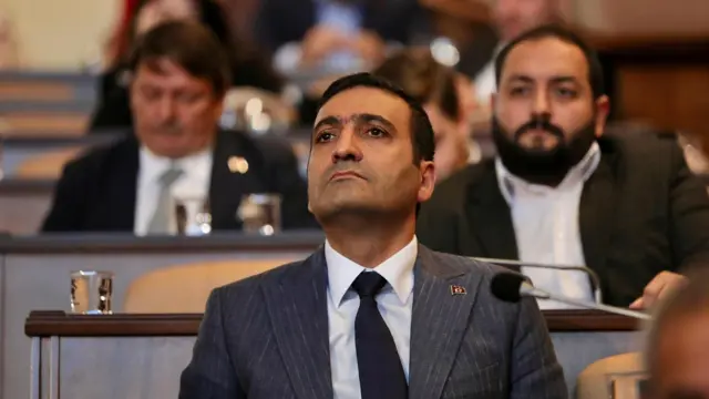 İnan Güney arkasında bazı diğer erkek üyelerin flu görüntüleri var, toplantıyı izliyor.