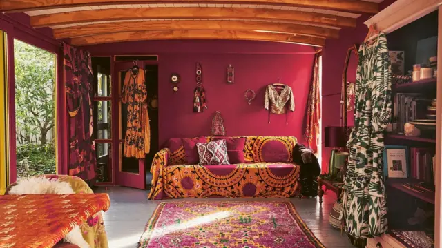 Fotografia colorida mostra uma sala com paredes rosa e roupas penduradas nas paredes e portas