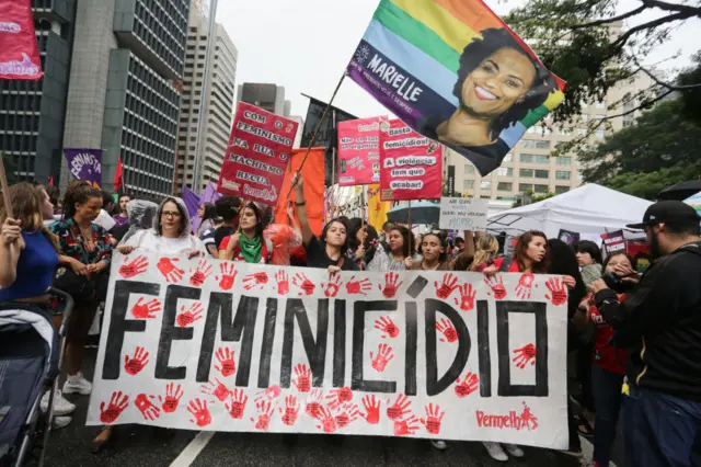 Mulheres seguram cartaz com a palavra feminicídio e fotogrupo do flamengo na libertadores 2024Marielle Francoem manifestação feministagrupo do flamengo na libertadores 2024São Paulo