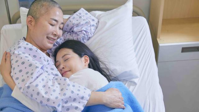 Mother with hair loss hugs her daughter in a hospital bed (stock shot of actors) 3453