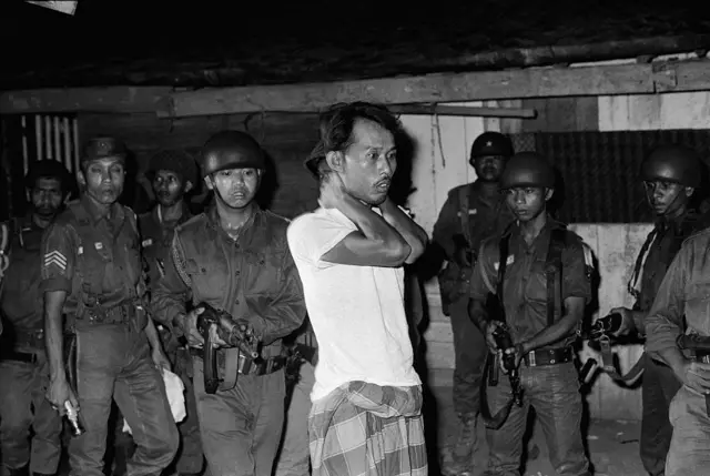 Seorang pria yang diduga sembagai simpatisan G30S ditodong senjata oleh aparat. Foto ini diambil pada 26 November 1965.