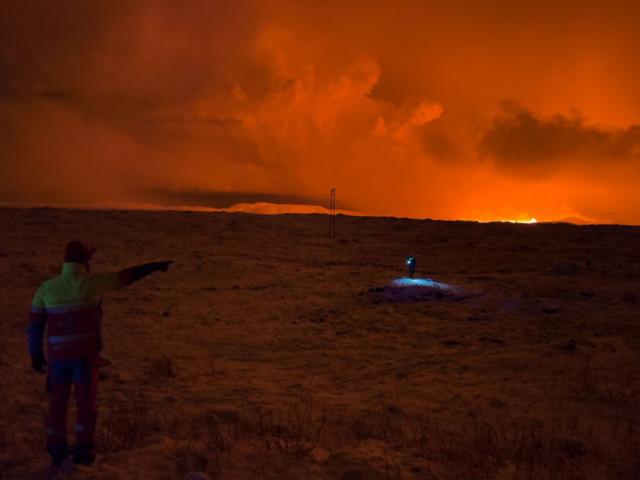 Una persona de pie señala en dirección al área donde un volcán hizo erupción en Islandia 