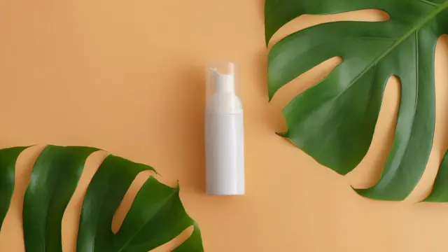 Blank cosmetics bottle on a table, a plant leaf on either side