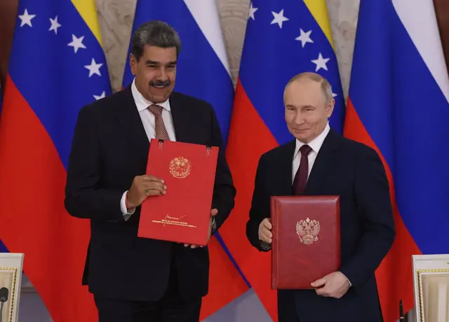 Nicolás Maduro y Vladimir Putin vestidos con trajes negros sonríen. Cada uno tiene en sus manos una carpeta roja.