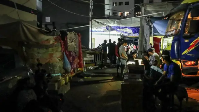 Tendas na escuridão com uma luz ao longe e pessoas conversando