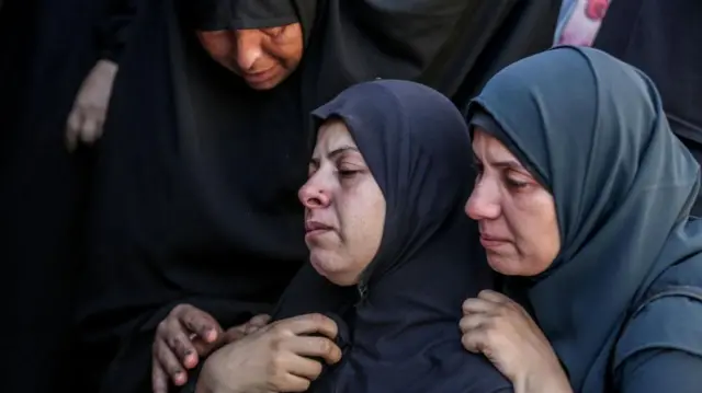 नुसेरत शरणार्थी शिविर पर हुए एक हमले में मारे गए लोगों के परिजन एक दूसरे को सहारा देते हुए