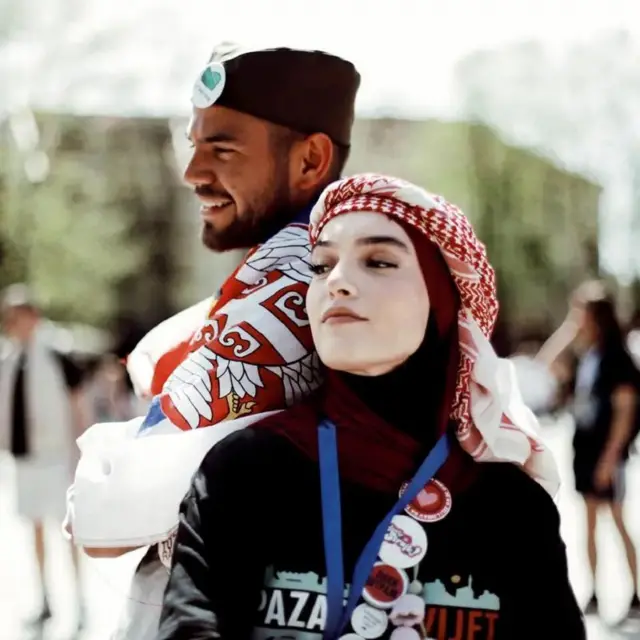 Devojka sa hidžabom na glavi i muškarac sa srpskom šajkačom na glavi