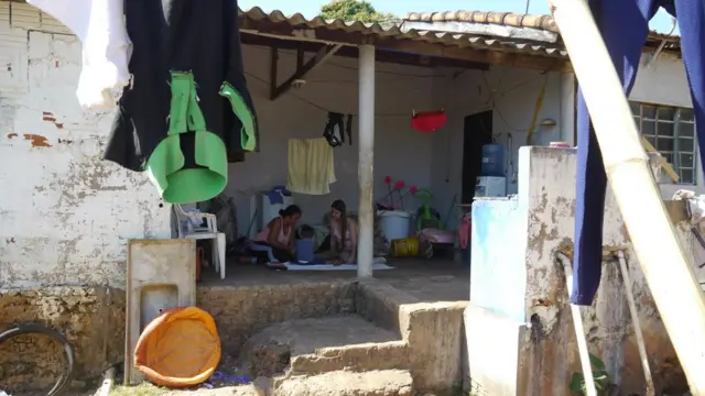 Mãe, criança e visitadora do Criança Feliz, sentadas no chão na varanda da casa (foto: Amanda Rossi/BBC Brasil)