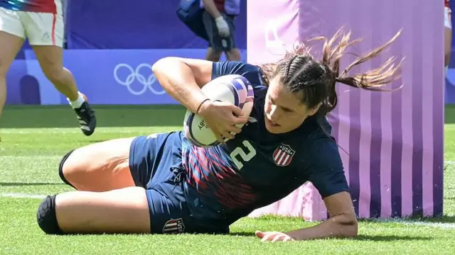 Ilona Maher, jogadora de rugby dos Estados Unidos, segura a bola deitada no chão em partida durante os Jogos Olímpicos de 2024, em Paris, na França