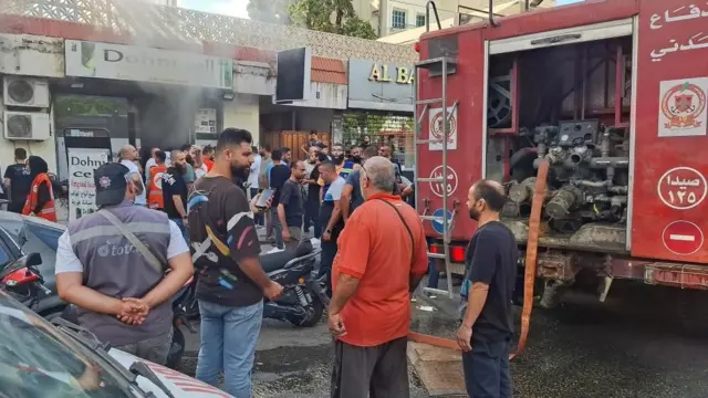 Des personnes se rassemblent alors que de la fumée s'élève d'un magasin mobile à Sidon, au Liban, le 18 septembre 2024.