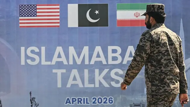 Un soldado pakistaní vestido con uniforme de camuflaje pasa junto a una valla publicitaria sobre las conversaciones de paz entre Estados Unidos e Irán en Islamabad.