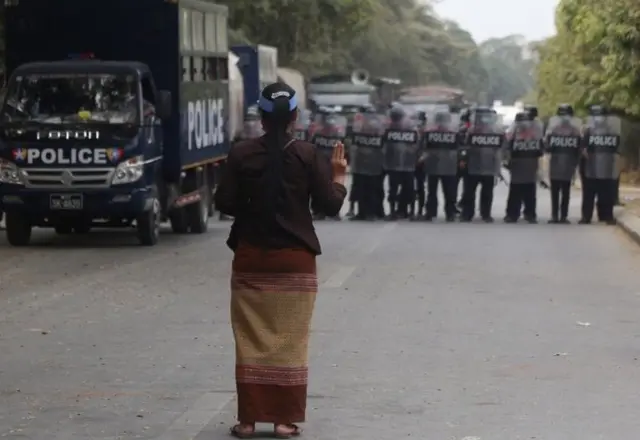 หญิงคนหนึ่งยืนชูสามนิ้วเผชิญหน้ากับแนวตำรวจ