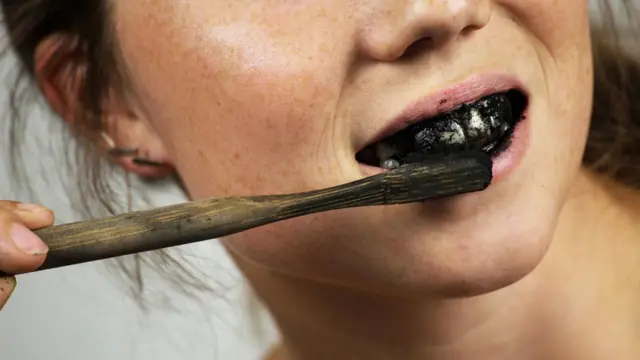 Young woman brushing her teeth with a black tooth paste with active charcoal