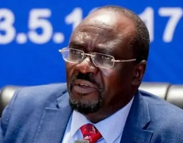 Profeseri Peter Kagwanja yambaye ikositimu y'ubururu, ishati y'ubururu hamwe na karuvati itukura, n'indorerwamo. 