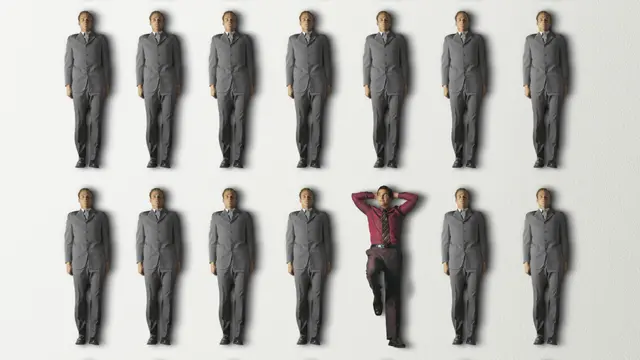 Una persona de camisa bordó y pose relajada entre filas de hombres de traje gris y pose rígida