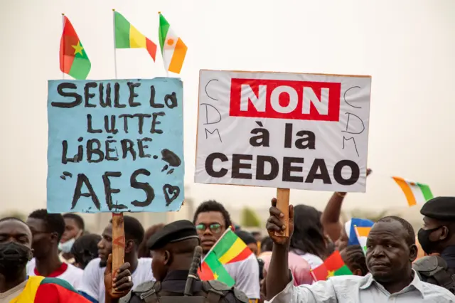 Des militants de l'AES brandissent des pancartes, l'une soutenant l'alliance du sahel, l'autre accusant la CEDEAO.
