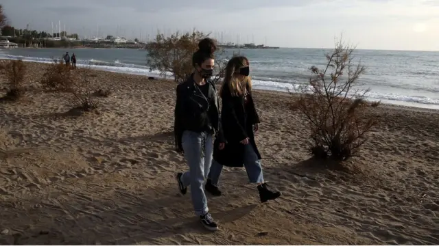 People wearing protective face masks walk on a beach during an unusual warm day in Athens
