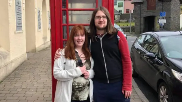 ایک سرخ فون بوتھ کے سامنے امیلیا اور لیوس ریلف کھڑے ہیں۔