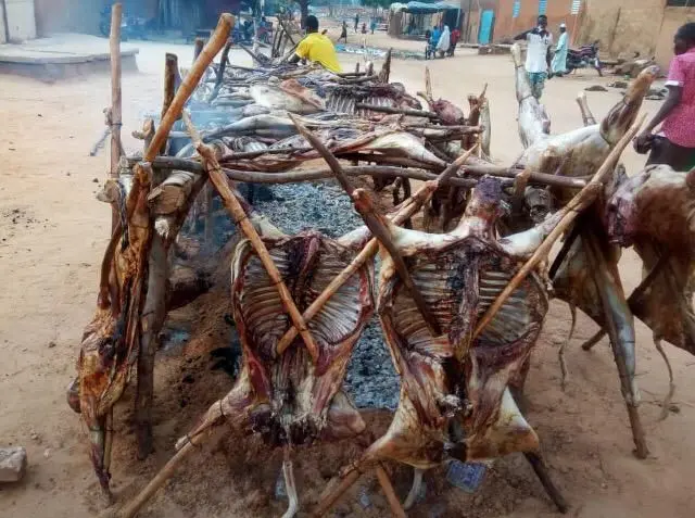 La viande est accrochée sur des piquets et posée sur la braise pour une cuisson lente.