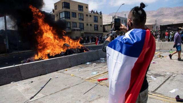 Hombre con la bandera de chile quemando ropa de migrantes