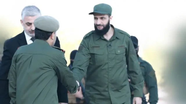 احمد شرع با لباس نظامی در حال دست دادن با یک نظامی