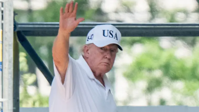 Trump saludando a la cámara con una gorra de USA.