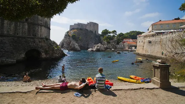Люди засмагають на невеличкому пляжі в бухті, на задньому плані - замок на скелі