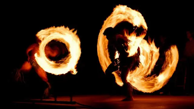 Dois dançarinos fazem apresentação com fogo em palco escuro