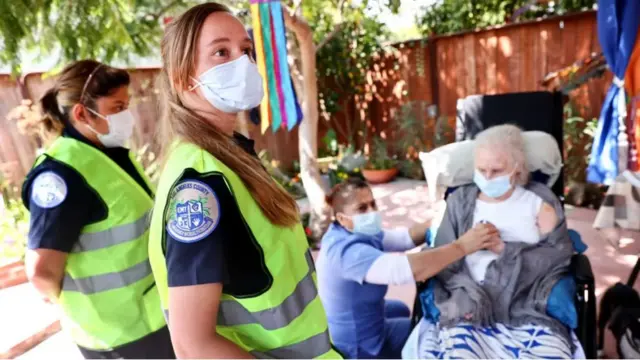 치매에 걸린 한 여성이 자원봉사자들의 도움을 받아 코로나19 예방 접종을 받고 있다