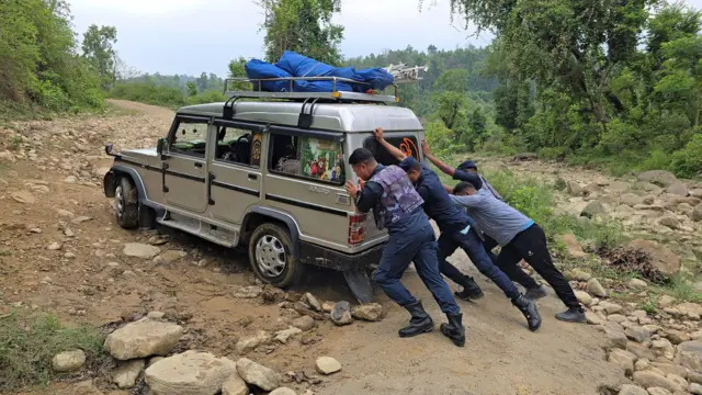 उकालो बाटोमा गाडी ठेल्दै प्रहरी र अन्य एक पुरुष