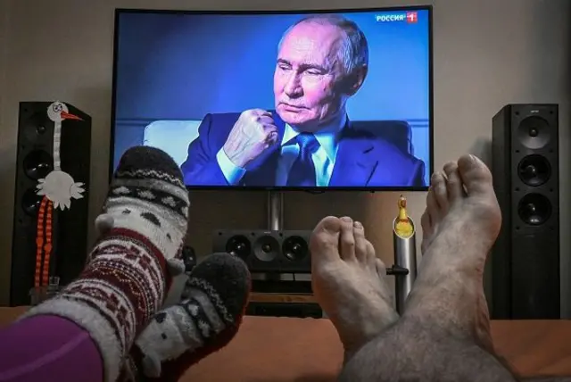 ноги у шкарпетках і без на тлі телевізора з Путіним 