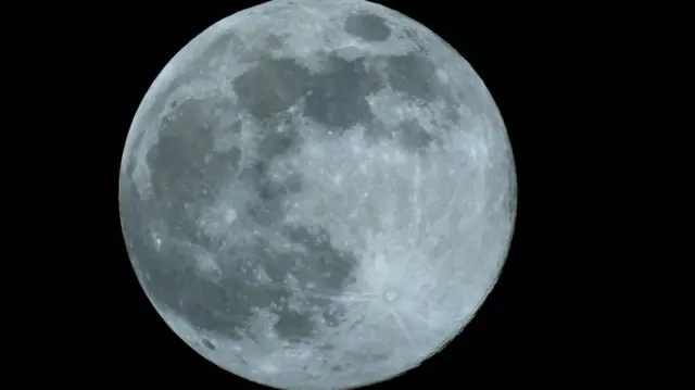 Un primer plano de la luna, que se ve gris contra un cielo negro.