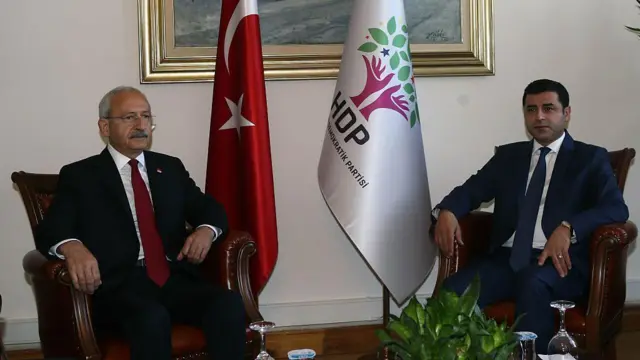 Karşılıklı koltuklarda oturmuş iki takım elbiseli erkek.
