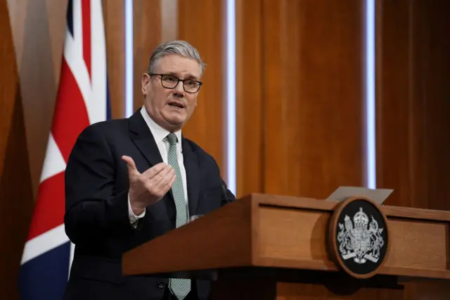 Стармер за трибуной, позади британский флаг.